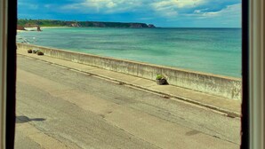 A coastal road with a concrete barrier, a clear sky, and a distant coastline.