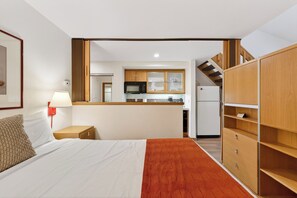 A hotel room with a bed, a nightstand, a lamp, a red wall-mounted phone, and a view of the kitchen area. - Ski-In/Ski-Out Condo • Pool, Hot Tub Access • Steps to KT-22 | The Traverse (Olympic Valley)