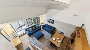 Un vaste espace de vie avec un canapé bleu, une table à manger en bois sur laquelle se trouve une assiette de nourriture, et un escalier menant à l’étage supérieur.