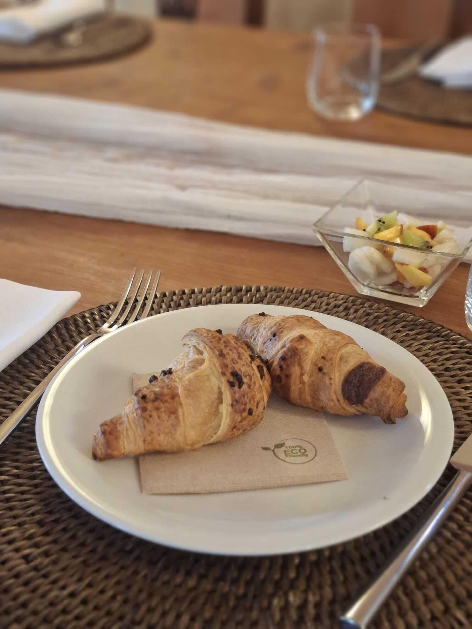A plate with two croissants and a small bowl of fruit on a table.