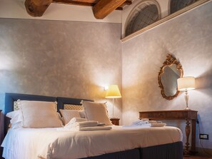 A bedroom with a bed, pillows, a nightstand, a lamp, a mirror, and a wooden ceiling. - CASALE DI VALLE DIMORA STORICA (Vinci)