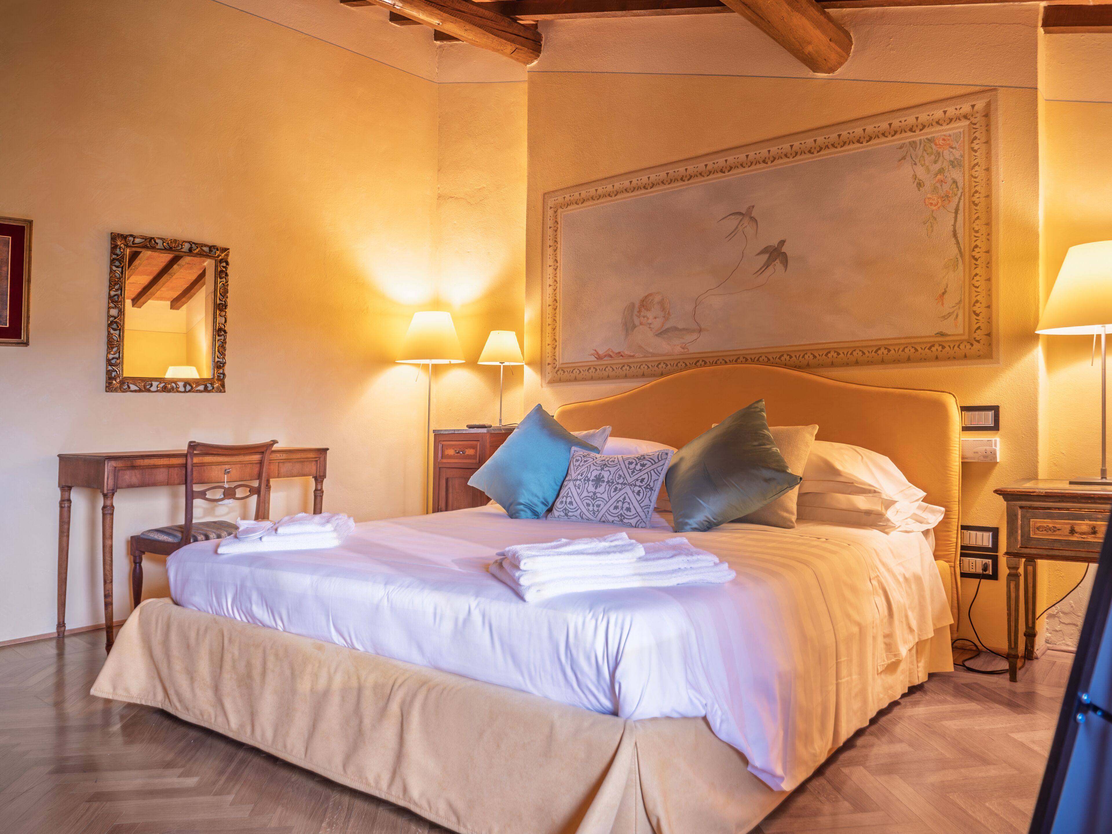 Un lit bien fait, avec des oreillers, un bureau en bois, une chaise et un grand tableau accroché au mur.