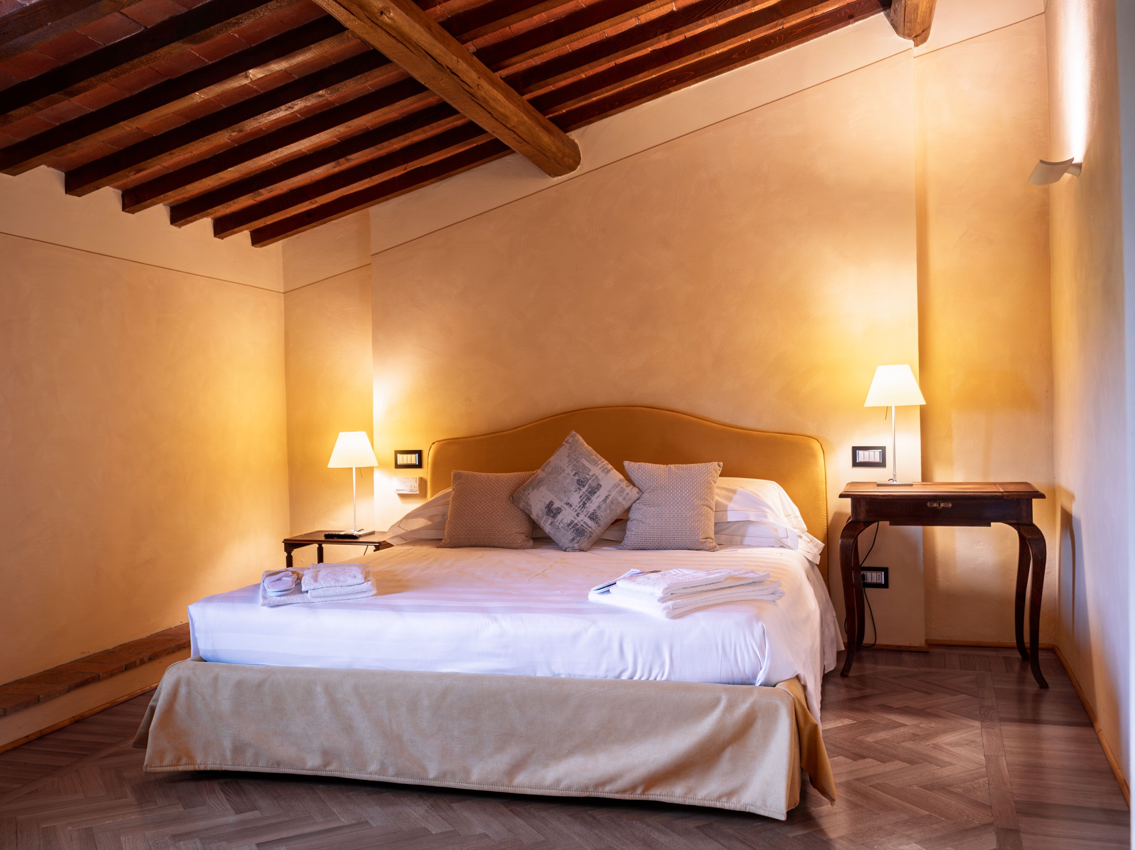 Une chambre d’hôtel avec un plafond en bois, un lit recouvert de draps blancs, deux lampes de chevet et une table de nuit en bois.
