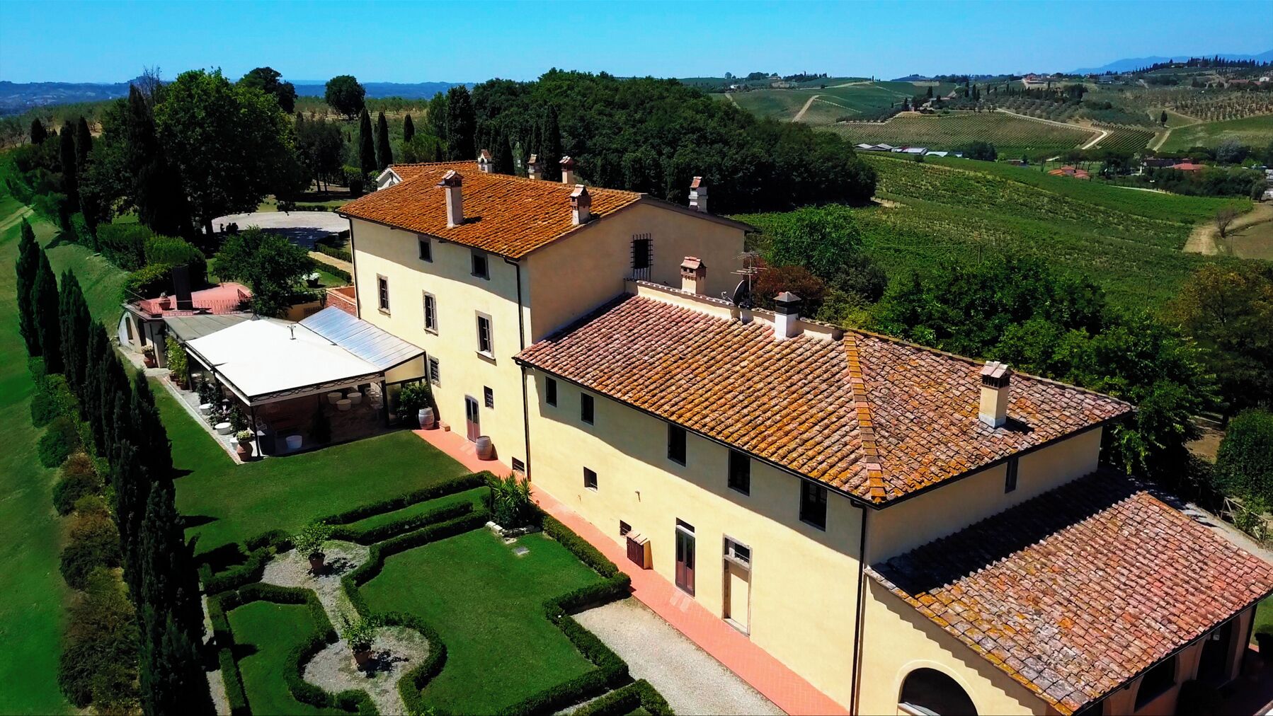 Un grand bâtiment à deux étages, doté d’un toit en tuiles, entouré de jardins et de vignobles bien entretenus.