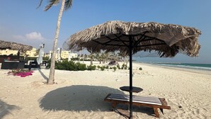 Ein Strand mit einer Strohdach-Sonnenschirm, einer Palme und einer Liege.