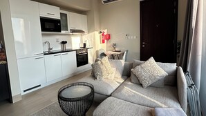 Ein modernes Wohnzimmer mit einer Couch, einem runden Couchtisch und einer Küchenzeile mit weißen Schränken und einer Mikrowelle.