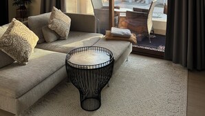 Ein modernes Wohnzimmer mit einer Couch, einem runden Couchtisch und Blick auf ein Gebäude durch große Schiebeglastüren.