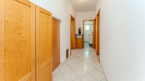 Un passadís amb portes de fusta, un paviment de rajoles i una petita planta sobre una estant.
