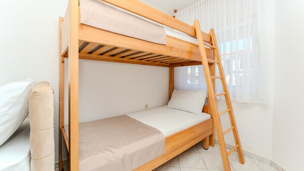 Un llit superposat amb escala, un llit individual i una finestra amb cortines.
