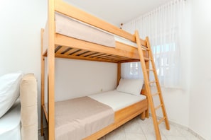 Un lit superposé avec une échelle, un lit simple et une fenêtre avec des rideaux.