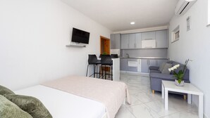 Una habitación de hotel moderna con cama, una mesita, un sofá, televisor, kitchenette y baño.