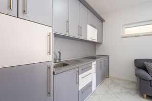 A modern kitchen with grey cabinets, a stainless steel sink, and a grey sofa.
