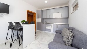 Un espacio habitable compacto con kitchenette, un sofá gris y dos taburetes negros.