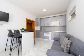A compact living space with a kitchenette, a grey sofa, and two black bar stools.
