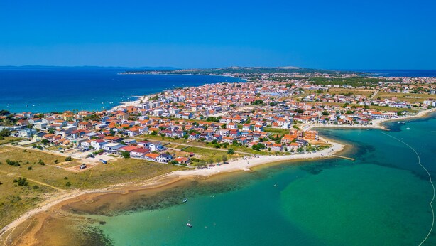 Vista aérea de un pueblo costero con una densa agrupación de edificios, una playa y aguas azul turquesa.