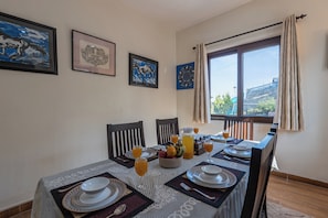 A dining area with a table set for four, featuring a fruit bowl, glasses, and a pitcher of orange juice. - Alaya Stays SnowPeak Vila With Hill View (Ranikhet)