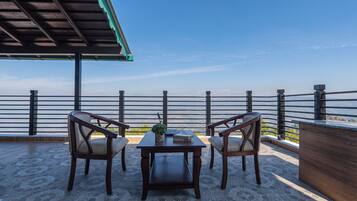 A terrace with a table and two chairs, a potted plant, and a view of the sea.