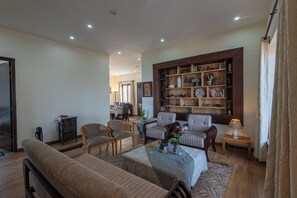 A living room with a sofa, chairs, a coffee table, and a bookshelf. - Alaya Stays SnowPeak Vila With Hill View (Ranikhet)