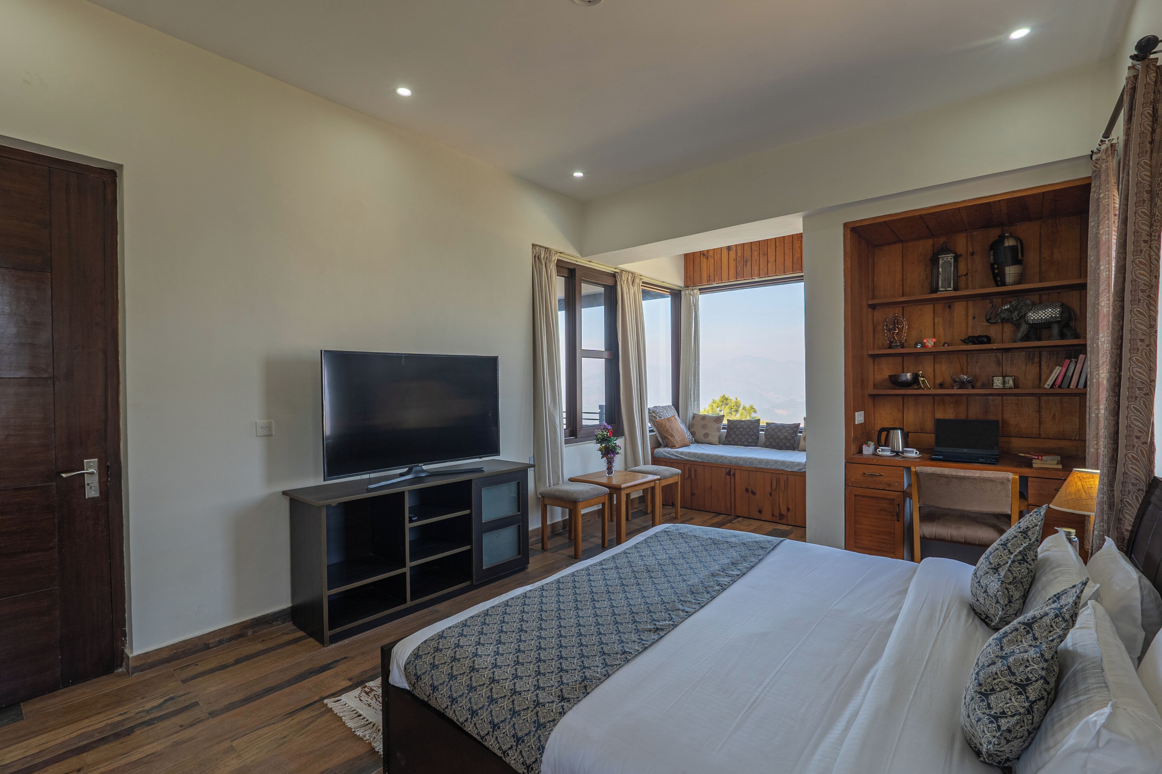 Une chambre d’hôtel avec un grand lit, une télévision, un bureau avec un ordinateur portable, une bibliothèque et une fenêtre avec des rideaux.