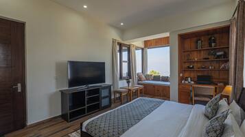 Une chambre d’hôtel avec un grand lit, une télévision, un bureau avec un ordinateur portable, une bibliothèque et une fenêtre avec des rideaux.