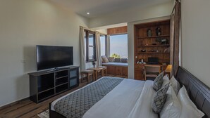 Een hotelkamer met een groot bed, een televisie, een houten bureau, een laptop en uitzicht op de omgeving.