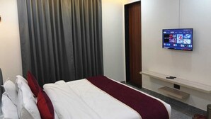 Ein Hotelzimmer mit Bett, Vorhängen, einem Fernseher an der Wand und einem kleinen Regal.