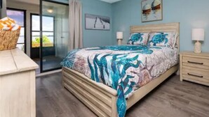 A bedroom with a bed, a nightstand, a dresser, a ceiling fan, and a sliding glass door leading to a balcony.