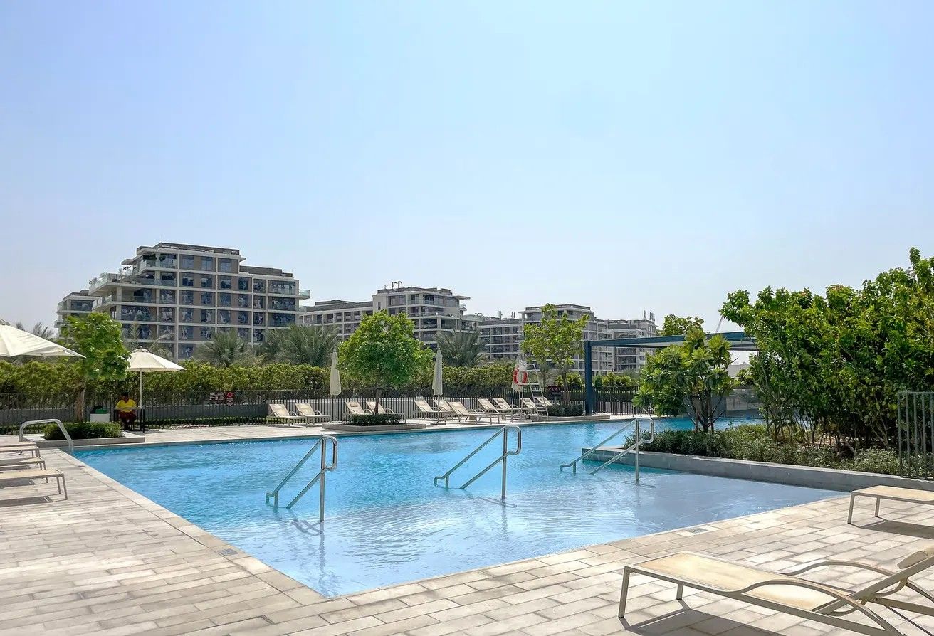 Une piscine entourée d’arbres et de bâtiments, avec des chaises longues et des parasols.