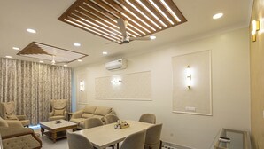 Ein modernes Hotelzimmer mit Essbereich, Deckenventilator, Einbauleuchten und einem großen Fenster mit Vorhängen.