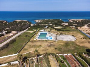 Vista aérea de uma propriedade com piscina, áreas ajardinadas e vista para o oceano.