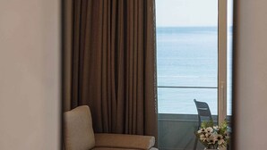 Una habitación de hotel con balcón, un sofá, una pequeña mesa con un jarrón y una silla.