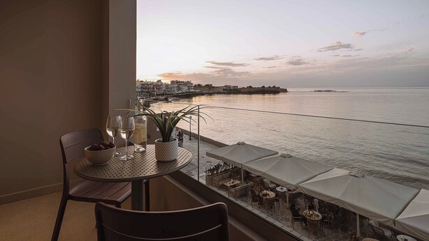 Un balcón con mesa, sillas, una planta en maceta y vistas al mar y edificios.