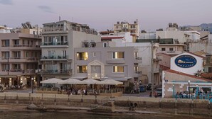 Un hotel frente al agua con asientos al aire libre, un letrero que muestra un barco y montañas, y vistas del agua.
