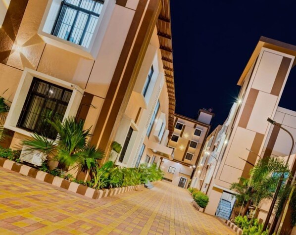 A nighttime view of a residential building with multiple floors, featuring balconies and a paved walkway.