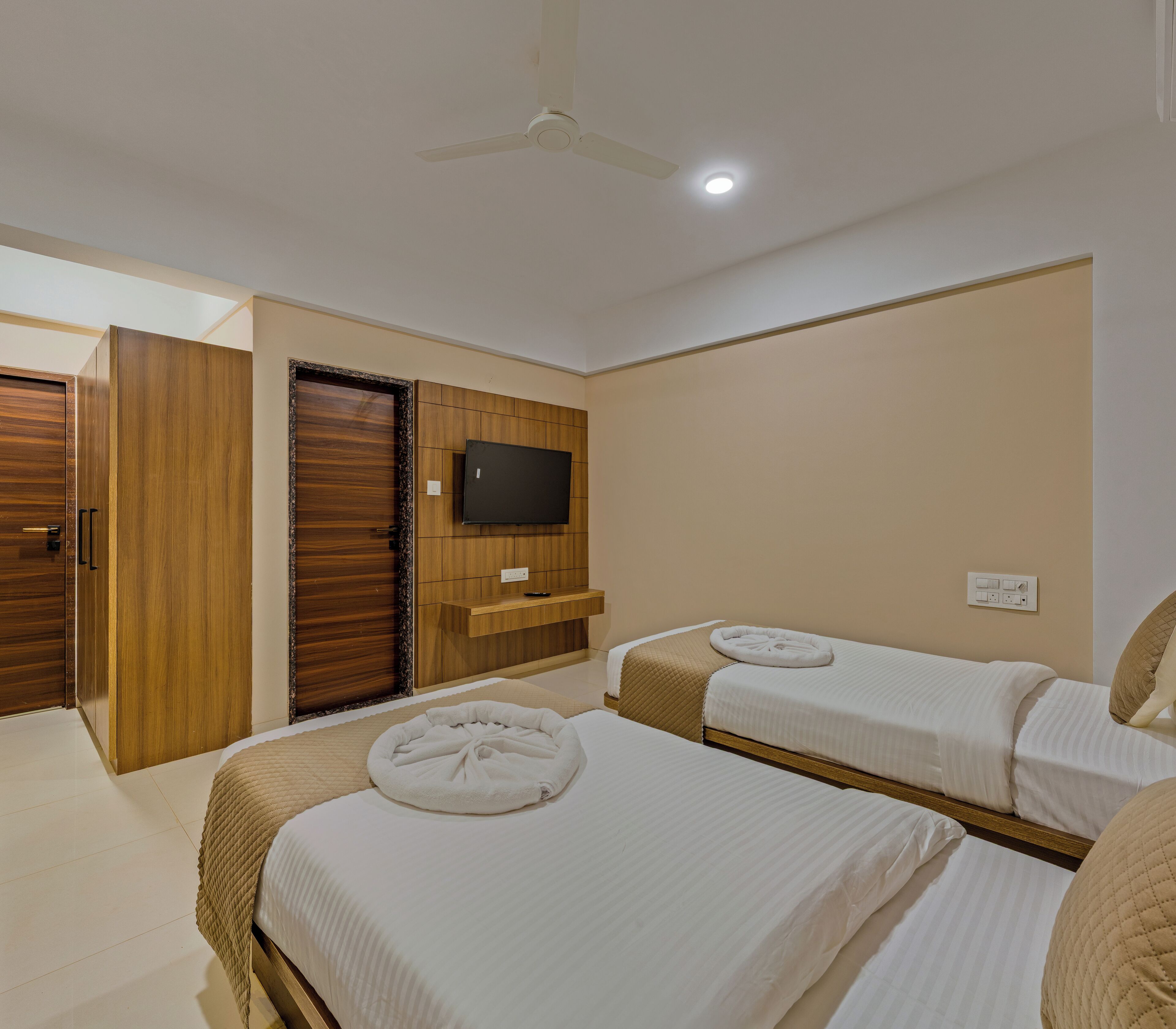 A hotel room with two beds, a TV, a ceiling fan, and a wooden wardrobe.