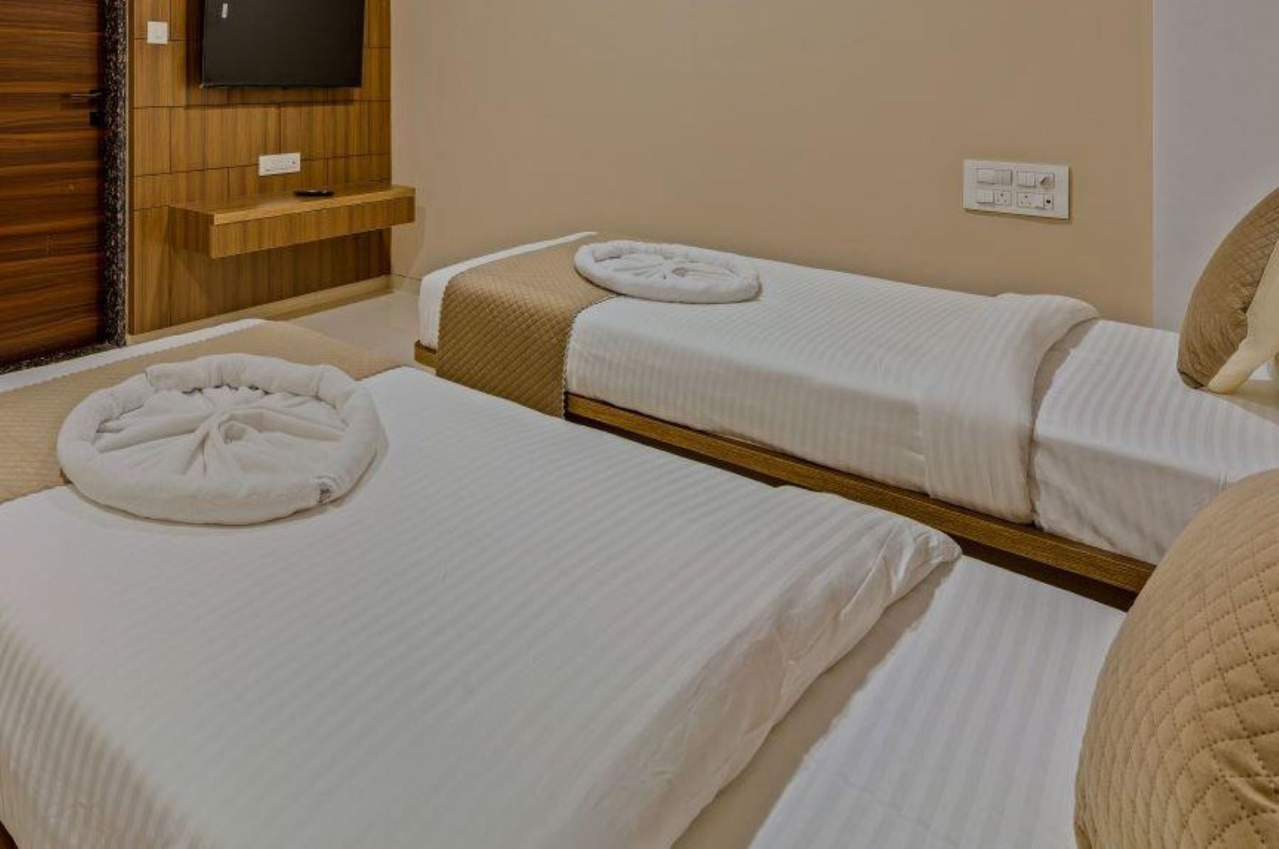 Quarto de hotel com duas camas de solteiro, uma televisão presa a um painel de madeira e uma tomada na parede.