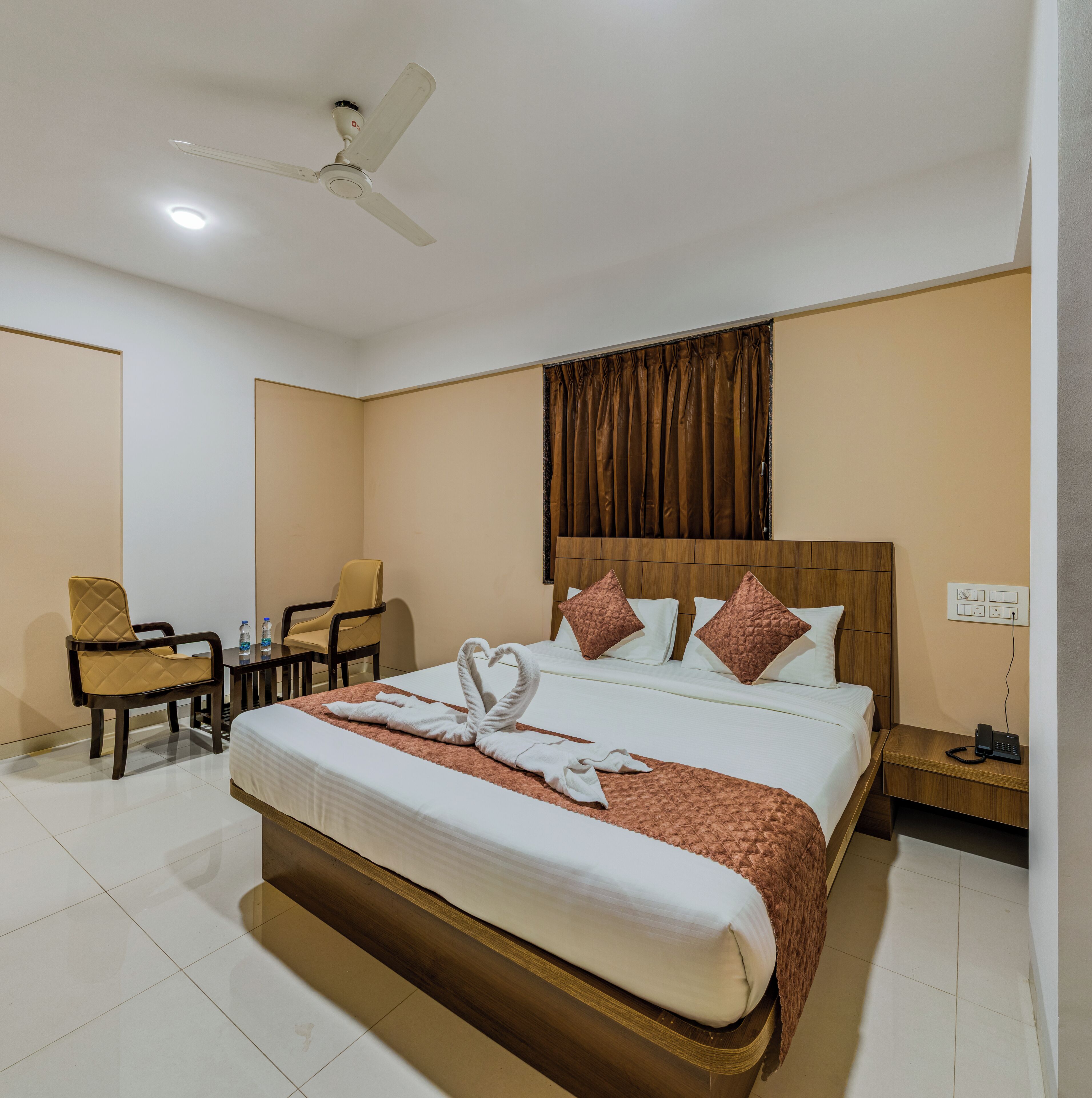 A hotel room with a bed, a desk, a chair, a ceiling fan, and a wall-mounted power outlet.