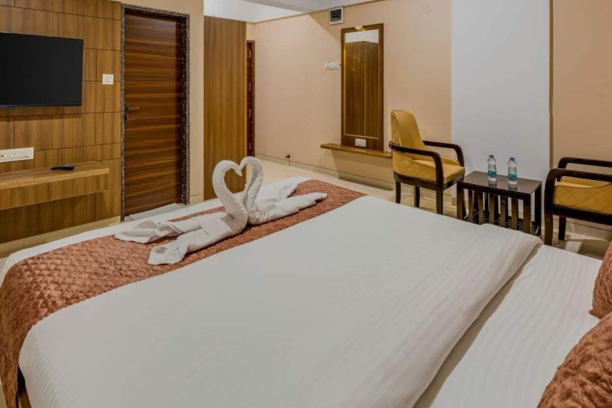 Une chambre d’hôtel avec un grand lit, un téléviseur fixé au mur, un bureau avec deux bouteilles d’eau et une chaise.