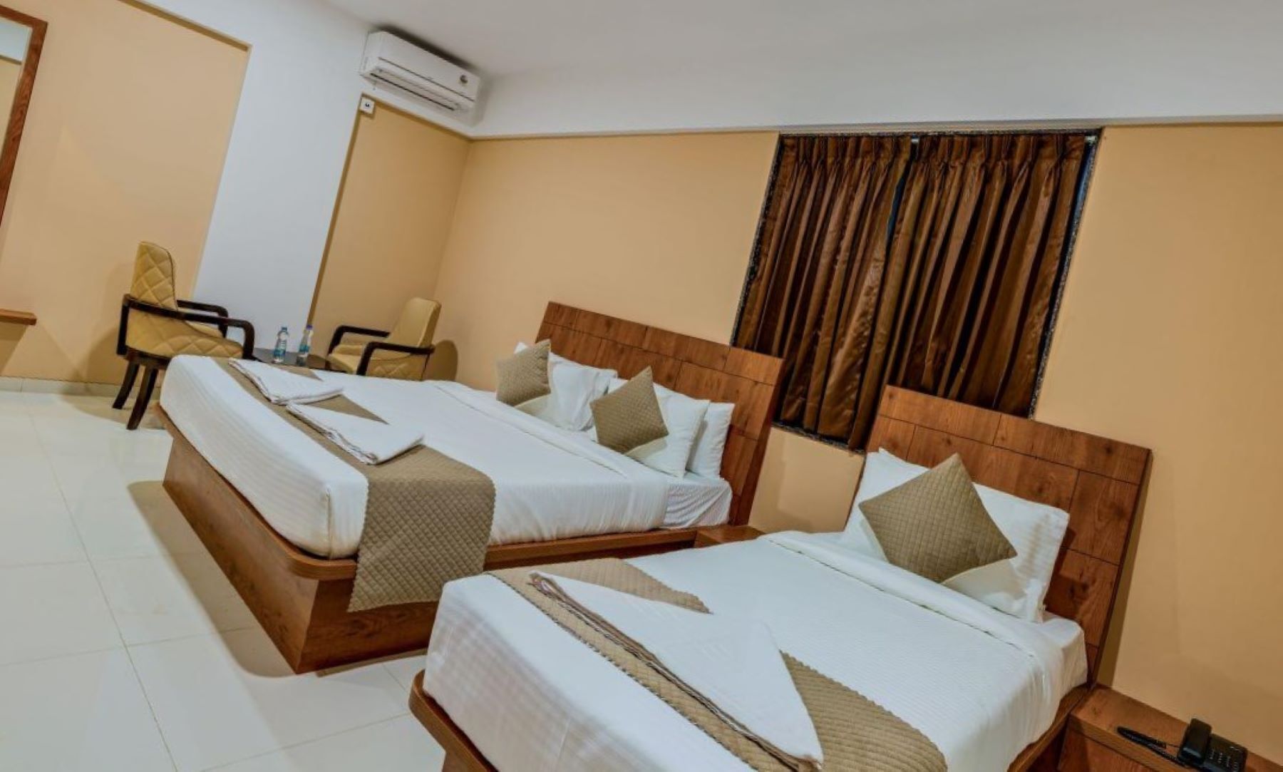 Une chambre d’hôtel avec deux lits, une chaise, une petite table et un appareil de climatisation.