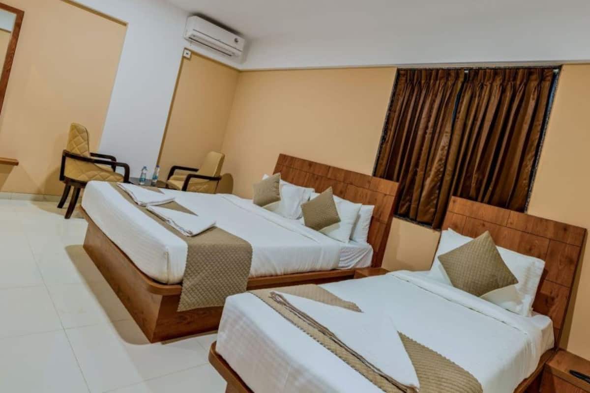 Une chambre d’hôtel avec deux lits, une chaise, une petite table et un appareil de climatisation.