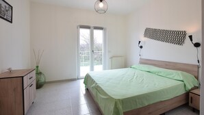 Un dormitorio con una cama, un aparador, un radiador, una lámpara fijada a la pared y una puerta que da a un espacio al aire libre.