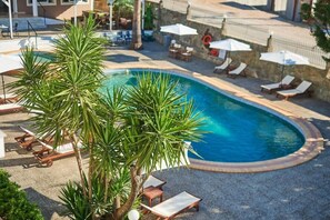A swimming pool with lounge chairs and umbrellas, surrounded by palm trees and a stone wall. - Armonia Hotel by Zante Plaza (Zakynthos)