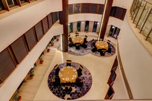 A multi-level atrium with two dining areas, each with round tables and chairs, surrounded by potted plants.