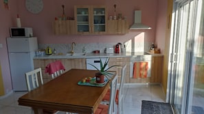 A kitchen with wooden cabinets, a white refrigerator, a microwave, a sink with a gold faucet, and a dining table with chairs. - House 200m from the beach, sea view, garden (Larmor-Plage)