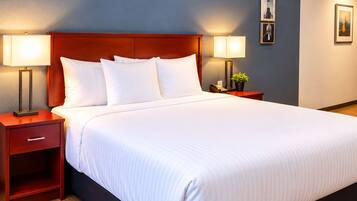 A hotel room with a large bed, two bedside tables, a nightstand, a lamp, a phone, and a small plant.