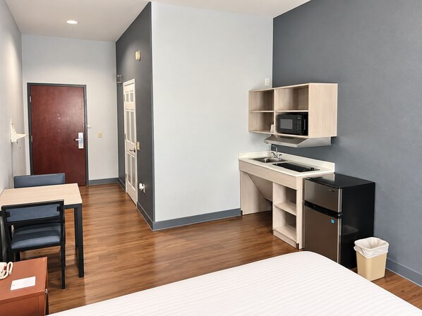 A compact hotel room with a kitchenette, a bed, a desk, and a chair.