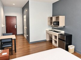 Habitación de hotel compacta con kitchenette, cama, escritorio y silla.
