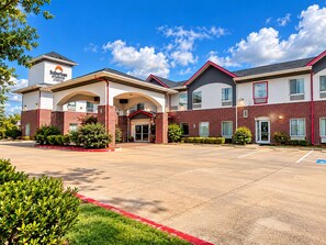 A Suburban Studios hotel with a central entrance, multiple parking spaces, and a clear sky.