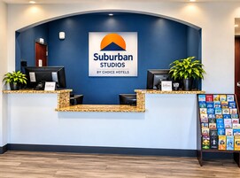 A hotel reception area with a blue wall, two reception desks, a welcome sign, a plant, and a book display.