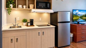 Eine moderne Küche mit einem Edelstahl-Kühlschrank, einer Mikrowelle, einer Kaffeemaschine und einem Fernseher auf einem Holzschrank.